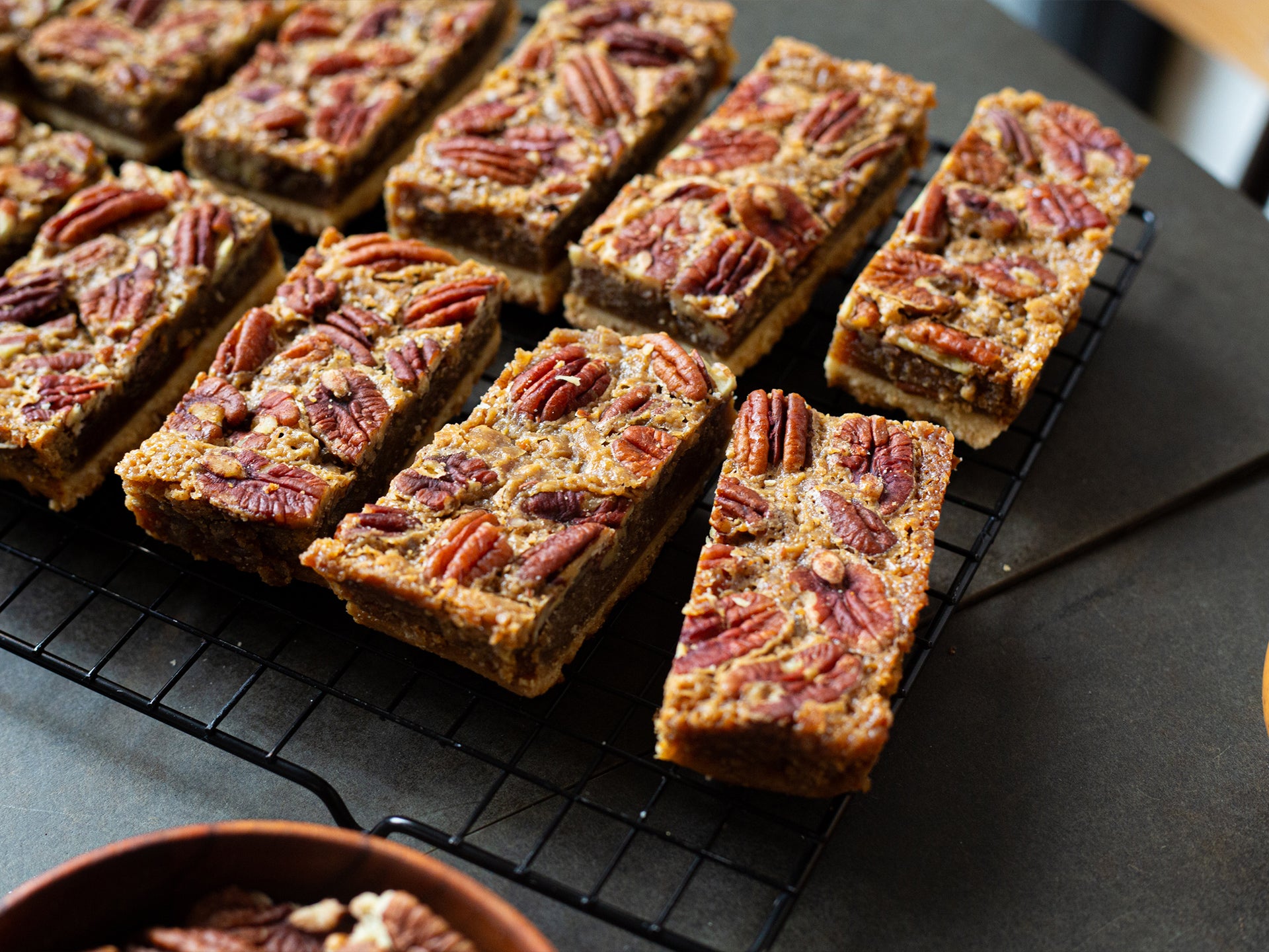 Wholesale maple pecan pie bars on a cooling rack with a bowl of pecans in the foreground
