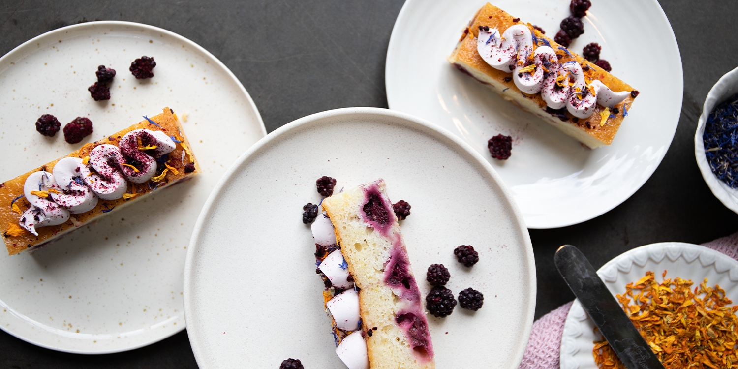 Slices of cake with berries and cream on white plates with a dark background