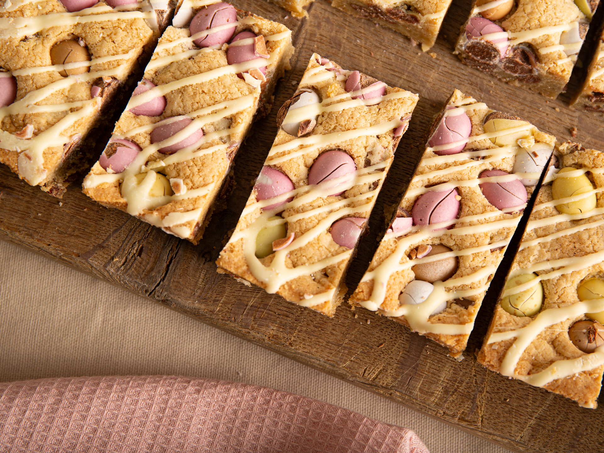 Sliced Mini Egg Cookie Bar with white chocolate drizzle and colorful candies on a wooden board.