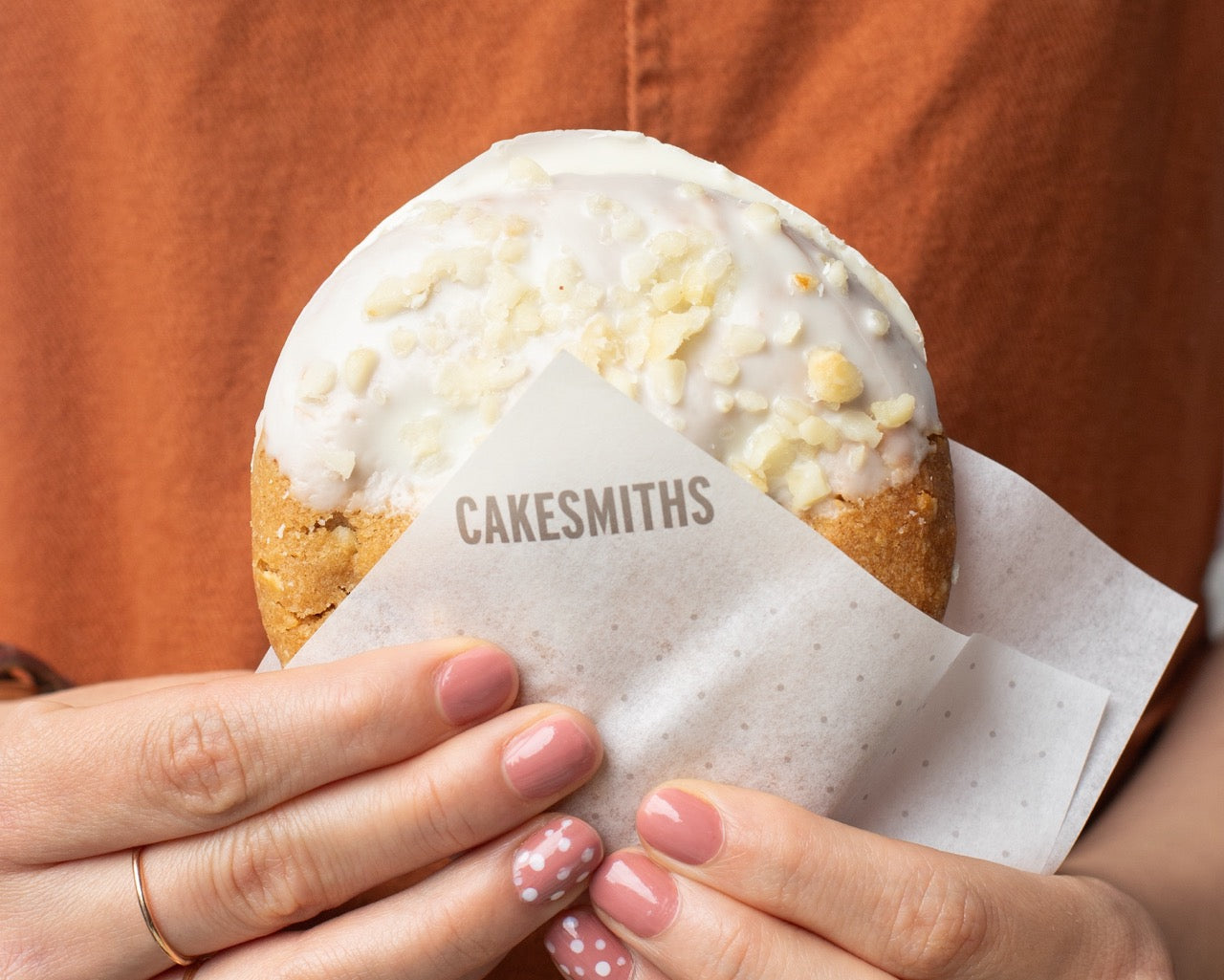 Miso Cookie with white glaze held by a person, wrapped in a 'CAKESMITHS' branded paper.