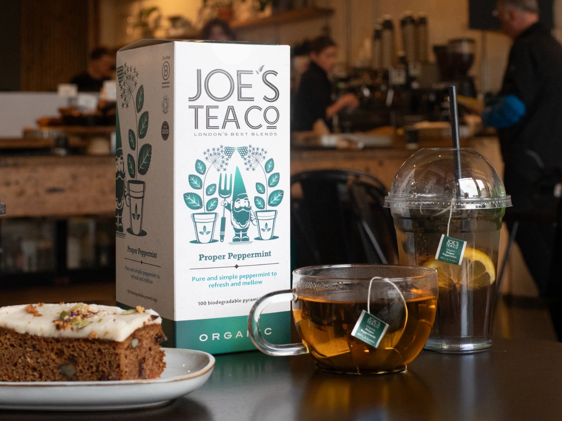 Joe's Tea Co - Proper Peppermint packaging with a cup of tea and cake on a table.