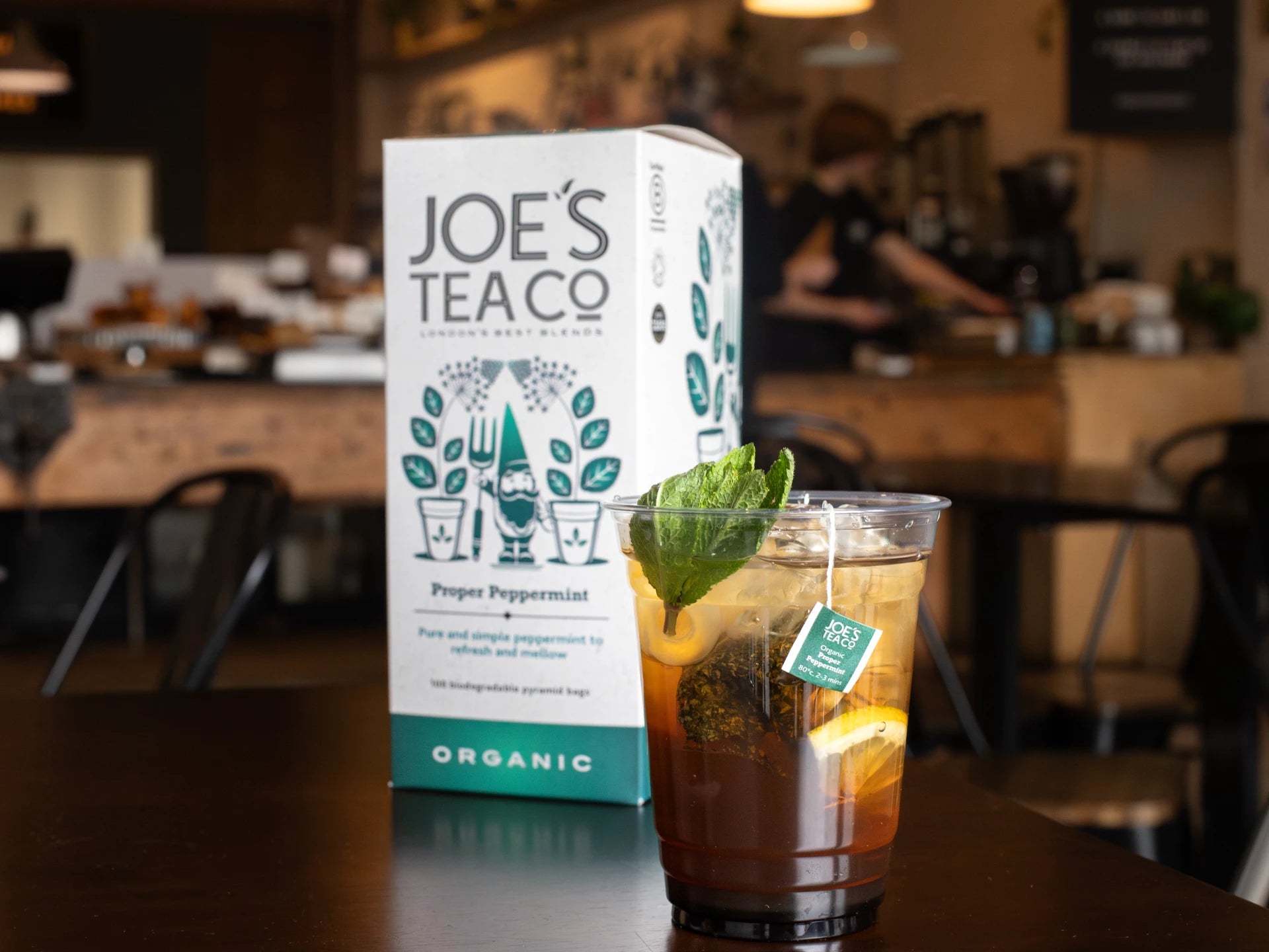 Joe's Tea Co - Proper Peppermint packaging with a iced tea in a cafe setting