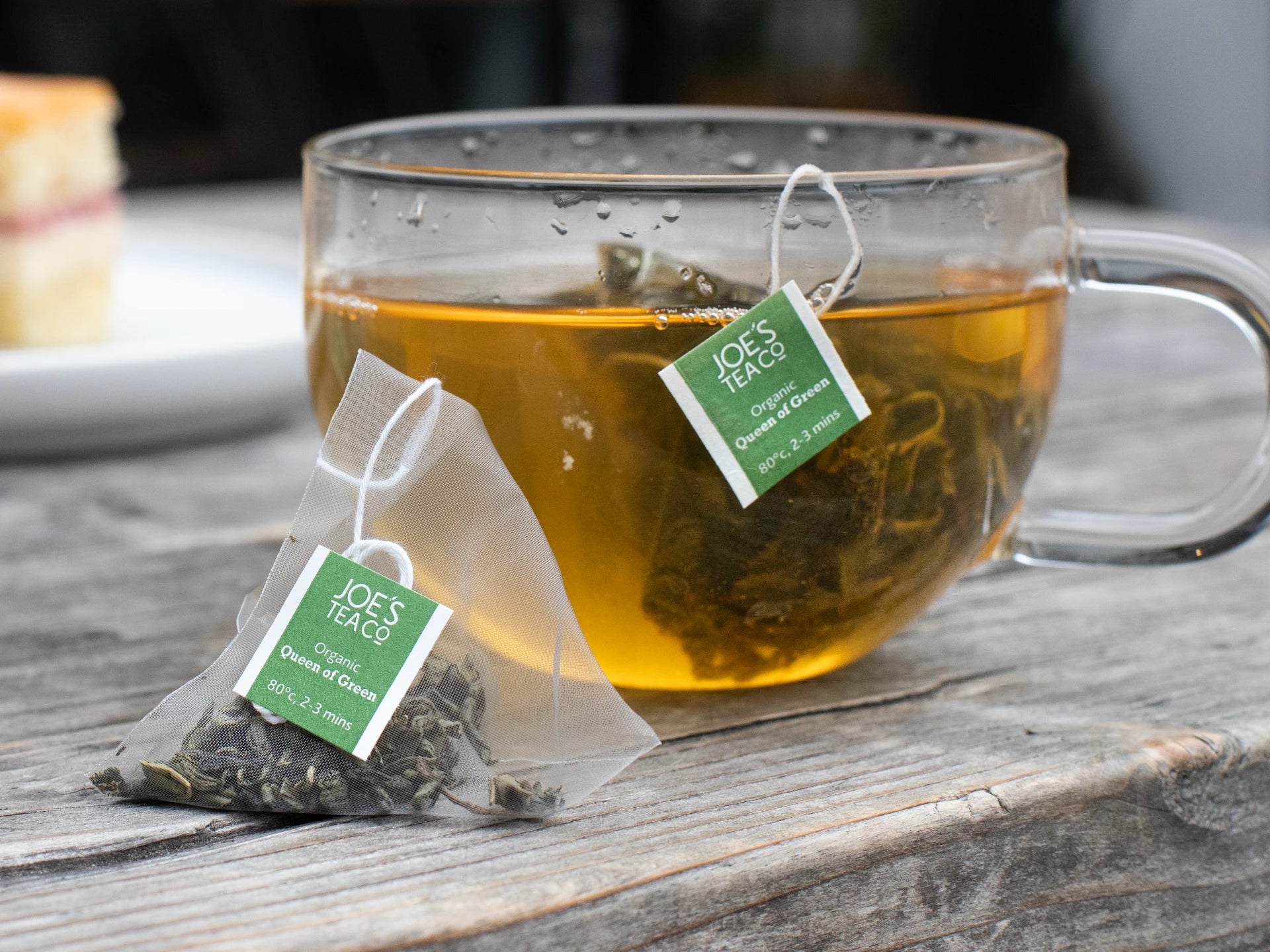 Clear mug of tea with JOE'S TEA bags on a wooden surface