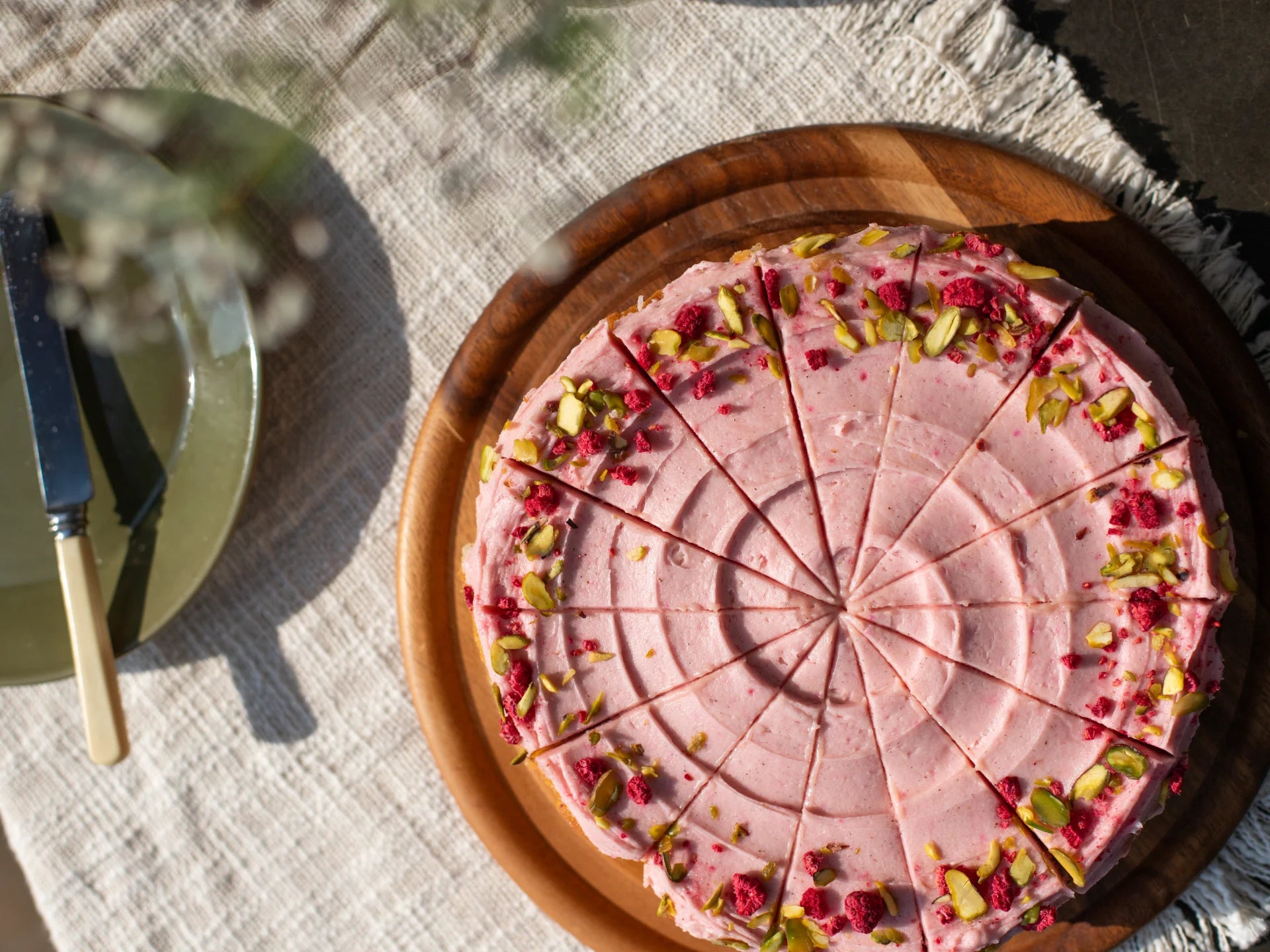 Pink Raspberry Rhubarb Cake  with green toppings on a wooden plate on a textured surface