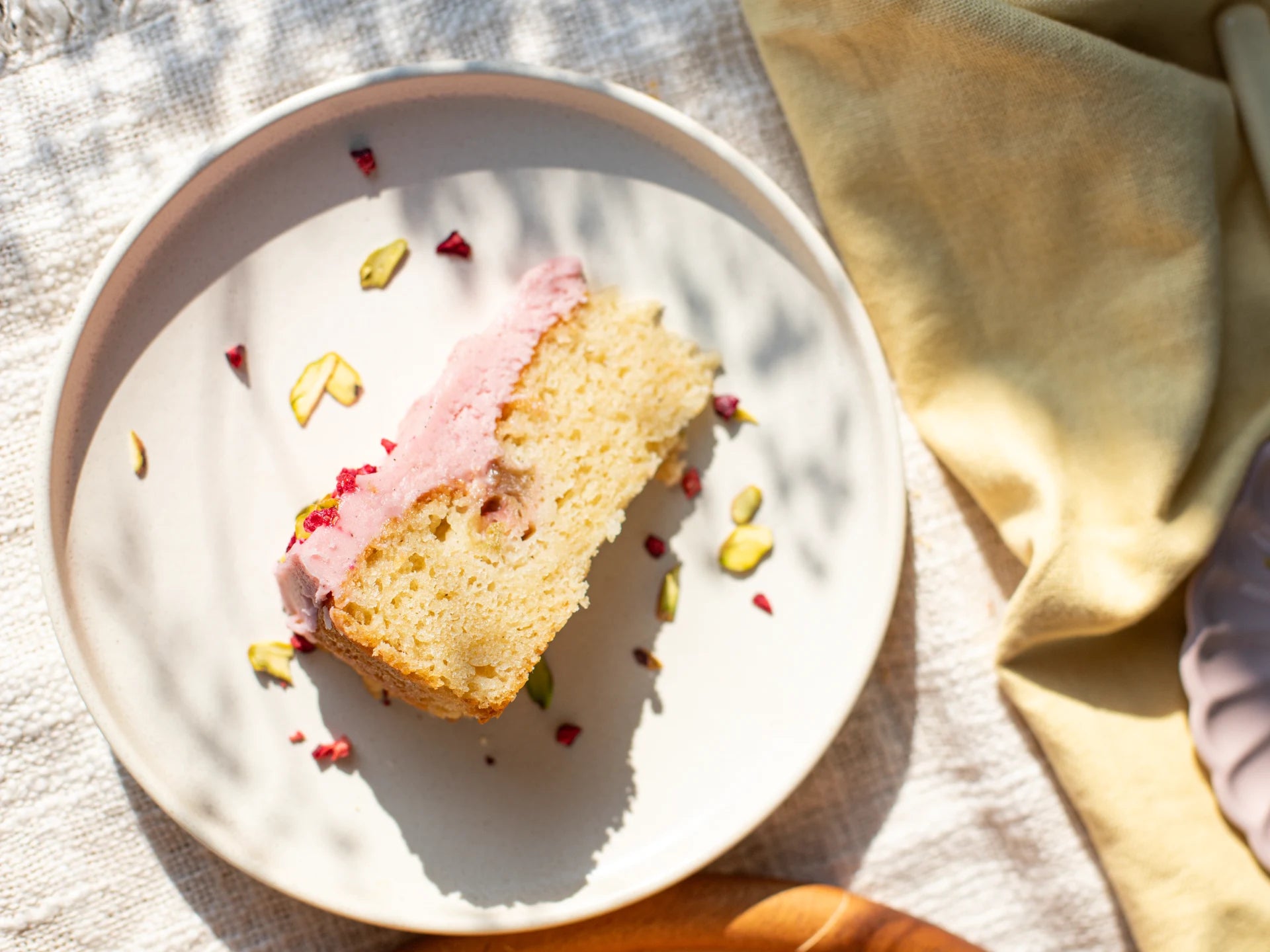 Slice of Raspberry Rhubarb Cake  with pink frosting on a white plate, yellow napkin in the background