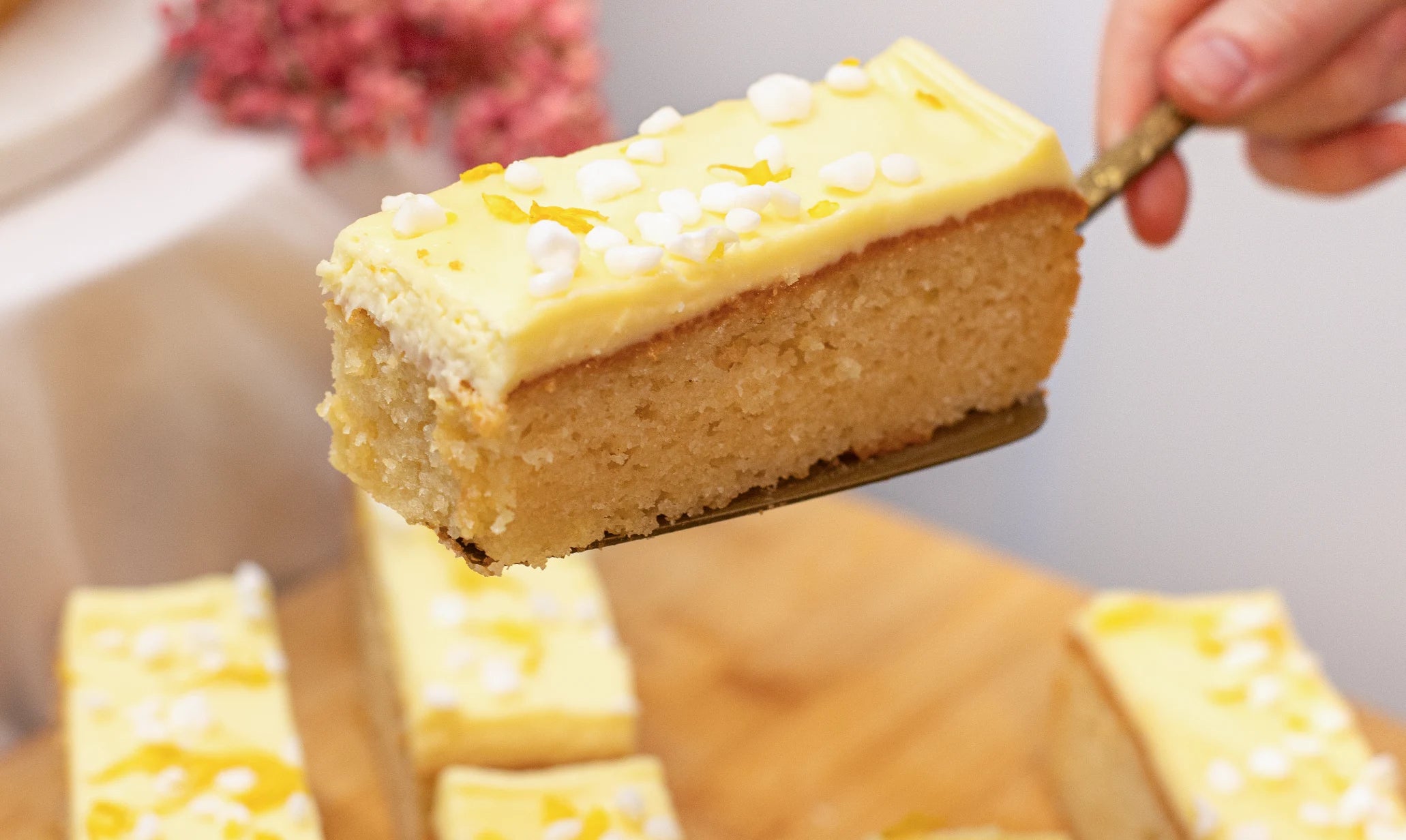 Slice of Sicilian Lemon Meringue cake being lifted with a spatula, surrounded by more cake slices on a wooden board.