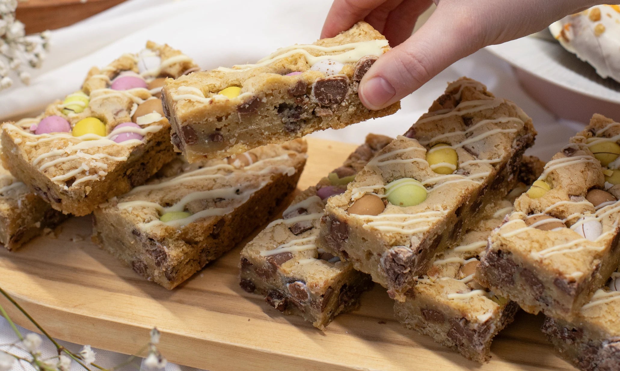 Slices of Mini Egg Cookie Bar with Easter candy on a wooden board, hand reaching for a piece.