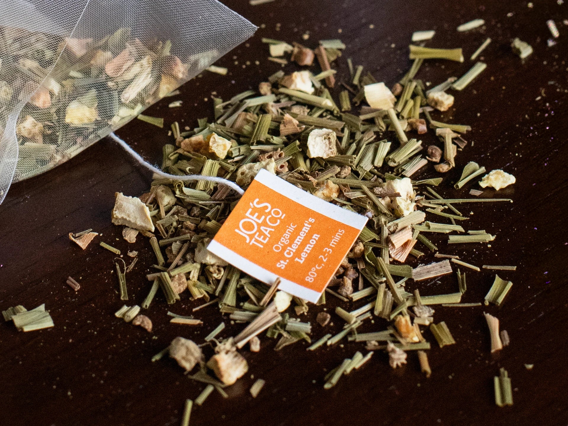 Joe's Tea co Tea leaves with a loose leaf tea bag on a dark surface