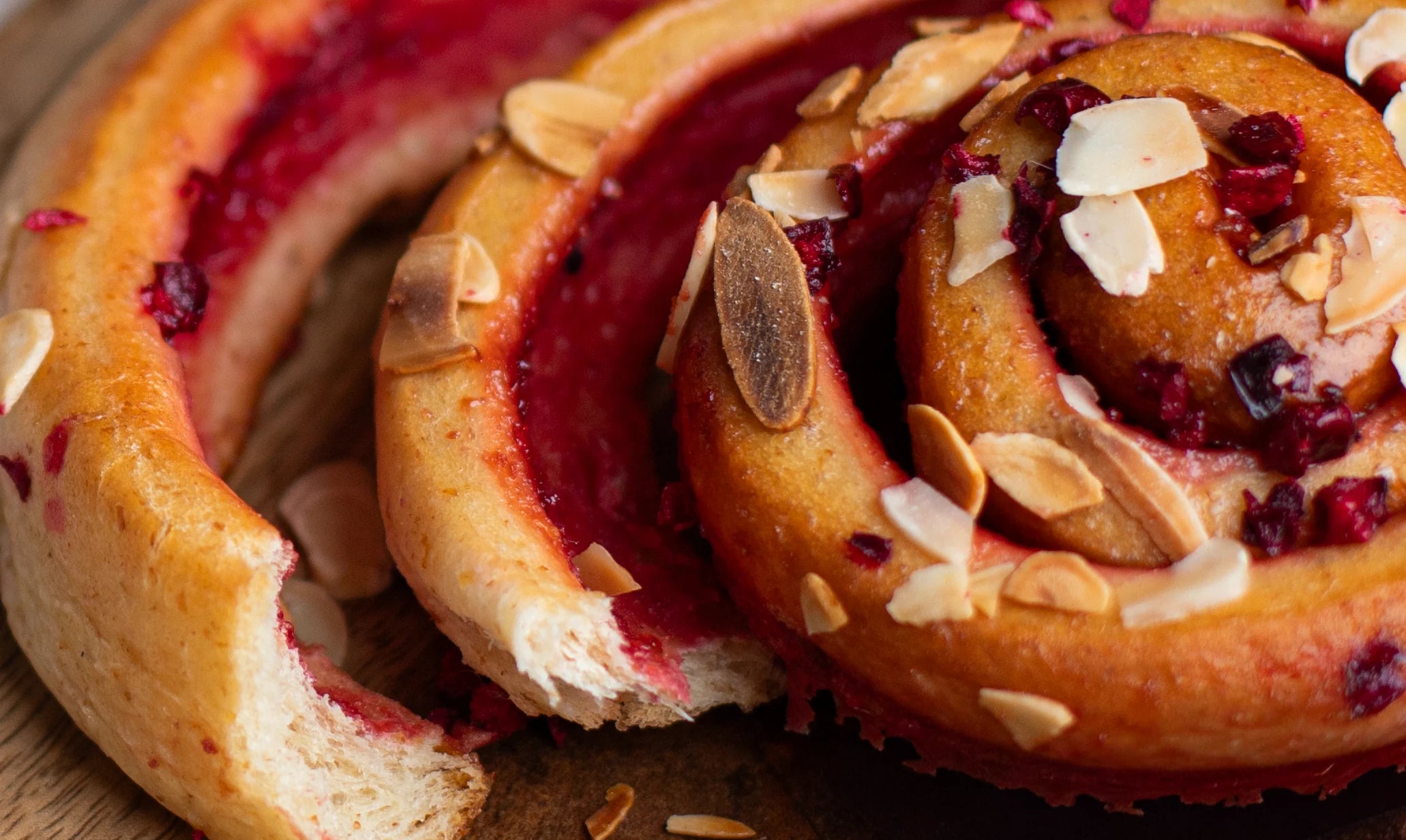 Close-up of a Sticky Cherry Bakewell Bun with raspberry filling and almonds on a wooden surface