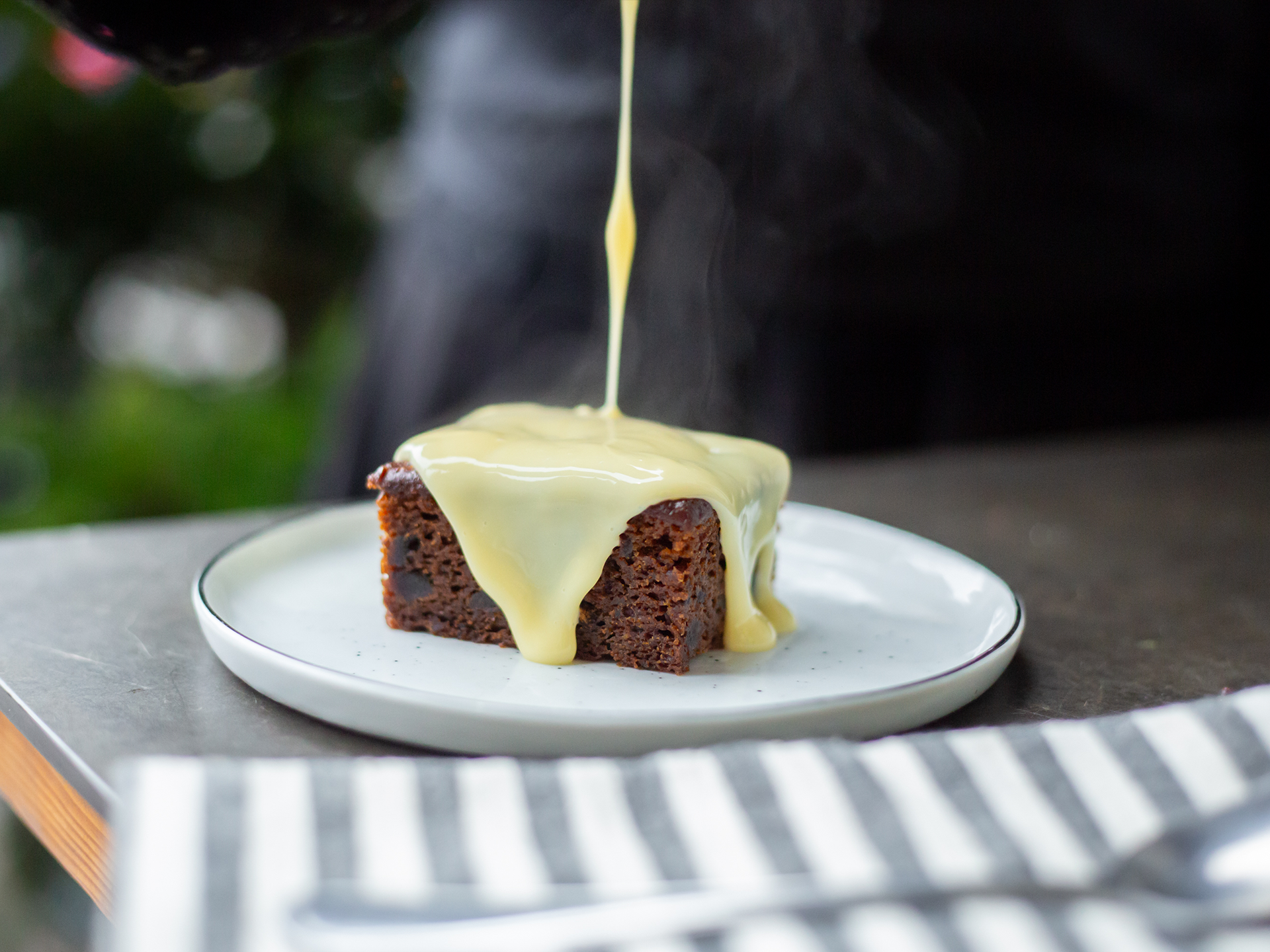 Slice of Sticky Toffee cake with a creamy topping being poured over it on a white plate.