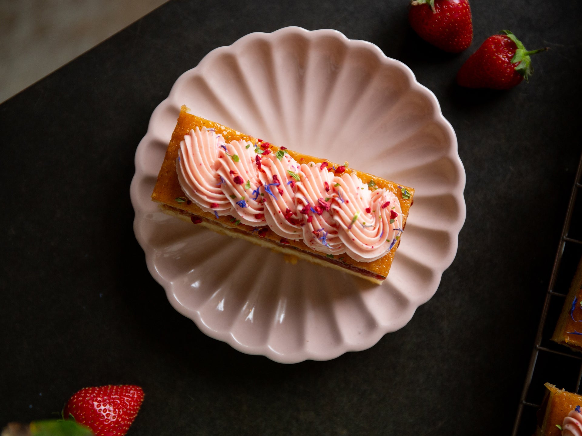 A slice of strawberry cake with pink frosting, served with more strawberries