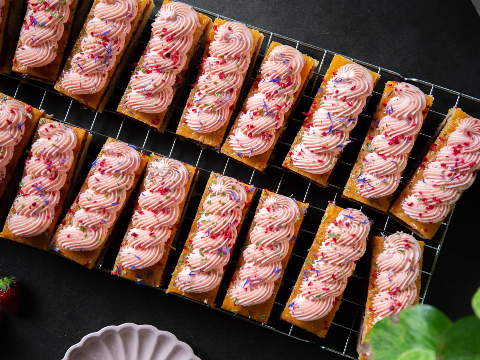 A tray of strawberry sponge, with piped strawberry frosting decorated with edible petals