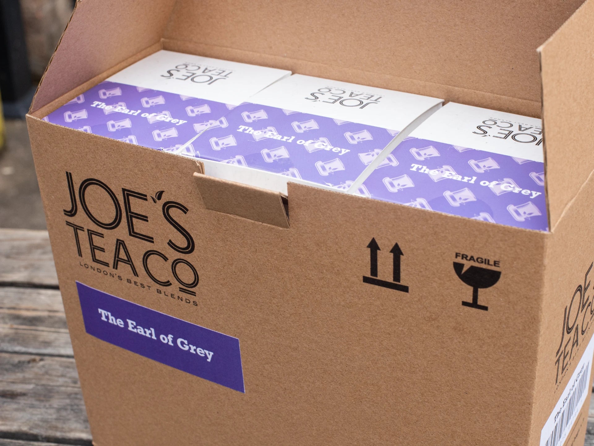 Cardboard box of Joe's Tea Co. The Earl of Grey tea packages on a wooden surface.