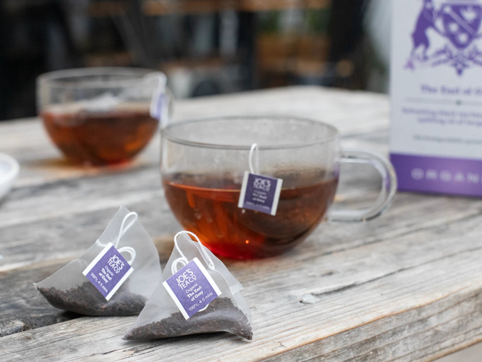 Tea bags and a glass mug with tea on a wooden surface, with a blurred background.