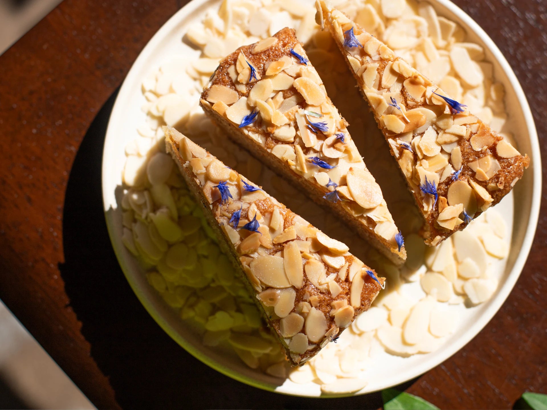 Three Honey Lavender Almond Round Cake slices on a white plate with almonds scattered around