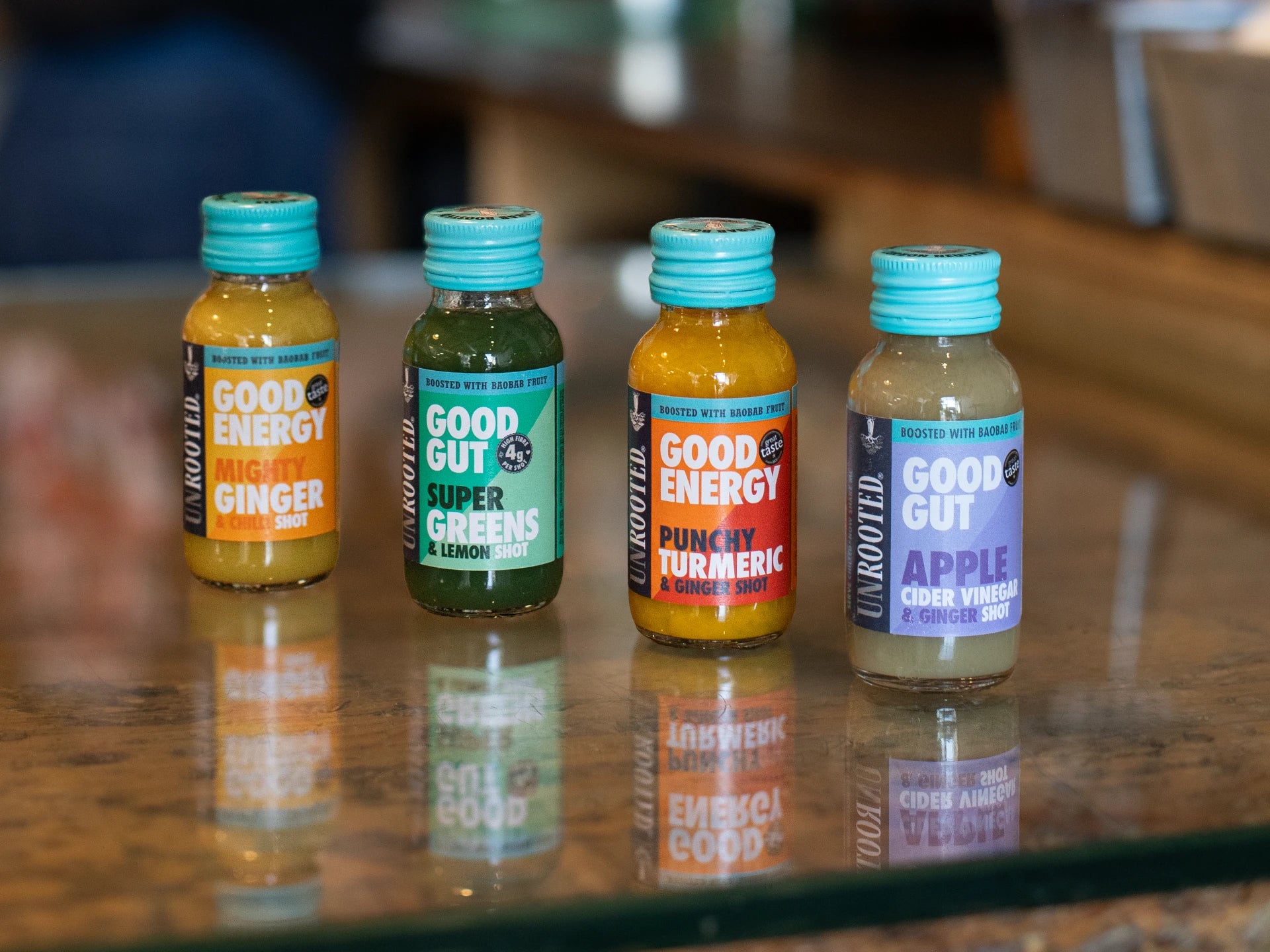 Four bottles of Unrooted Health Shots drinks on a glass countertop with a blurred background.