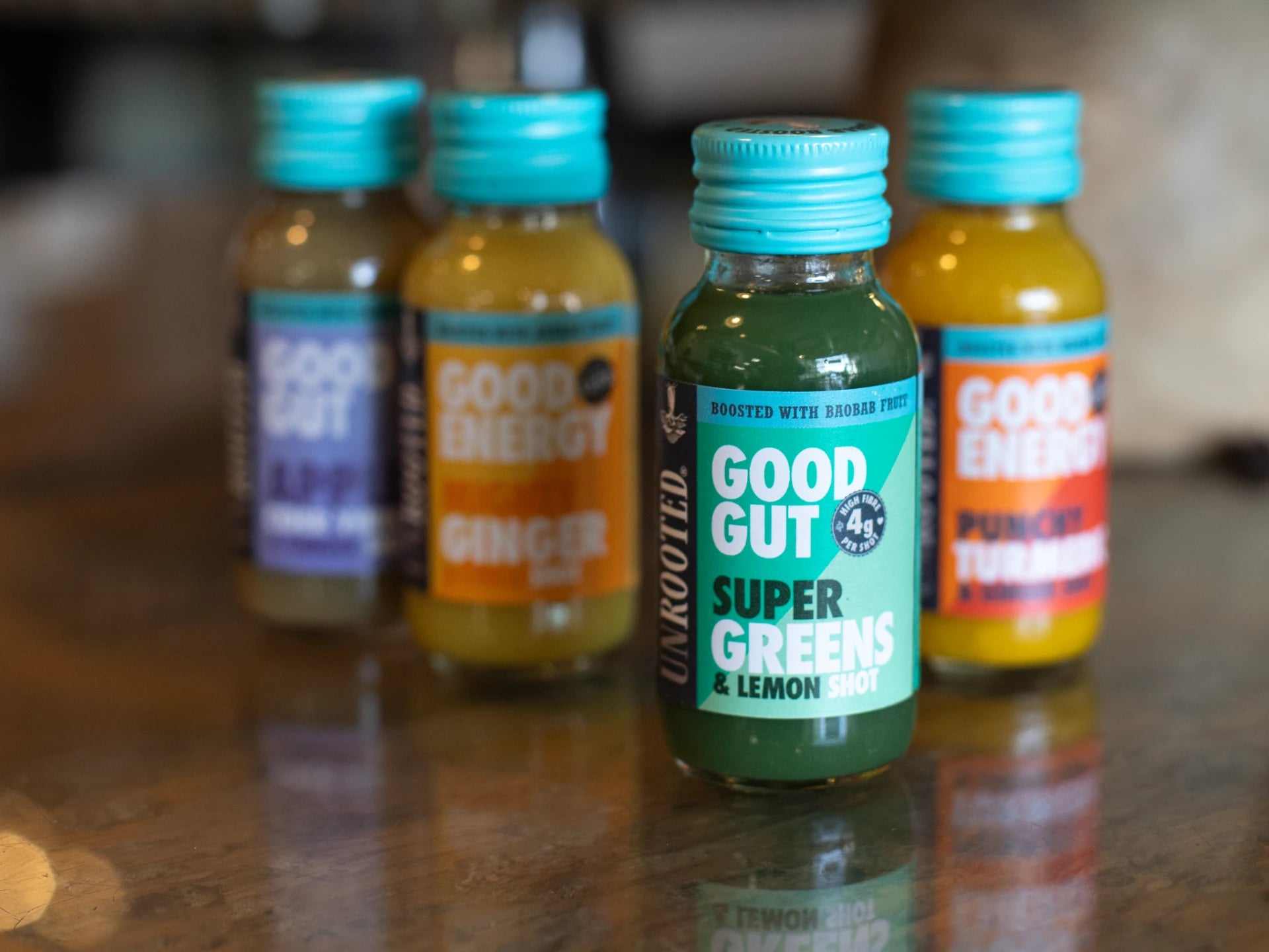 Unrooted Health Shots 'Super Greens' and 'Good Energy' supplements on a reflective surface with a blurred background.
