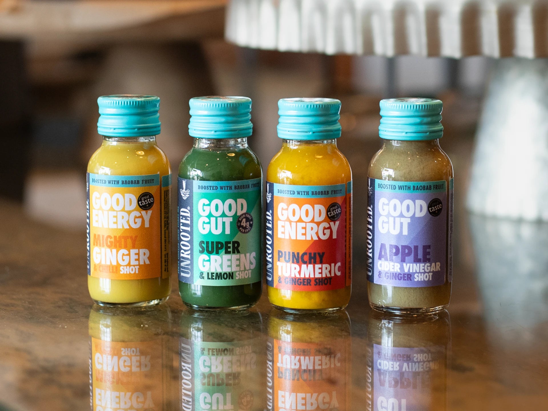 Four bottles of Unrooted Health Shots on a reflective surface with a blurred background.
